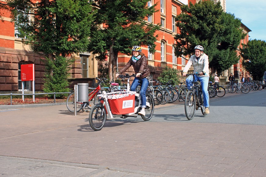 Eine Frau und ein Mann fahren auf dem Fahrrad in der Hochschulstraße. Die Frau fährt ein neues E-Lastenfahrrad der Marke KARGON.